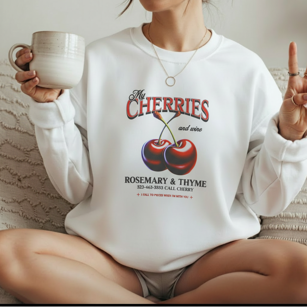 Woman wearing white My Cherries vintage graphic sweatshirt sitting on bed with coffee mug