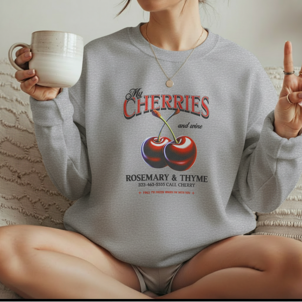 Woman wearing light grey My Cherries vintage graphic sweatshirt sitting on bed with coffee mug
