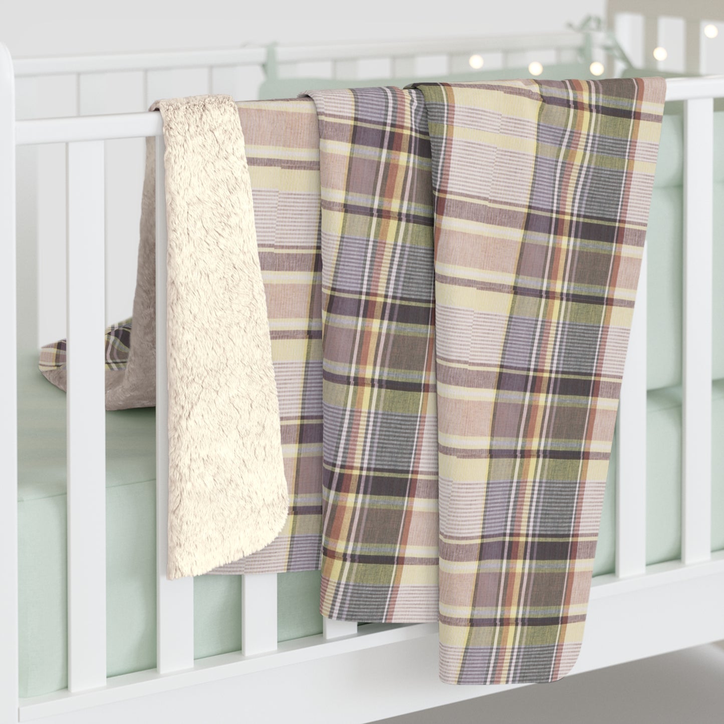 Plaid blanket draped over a white crib with a textured blanket on top
